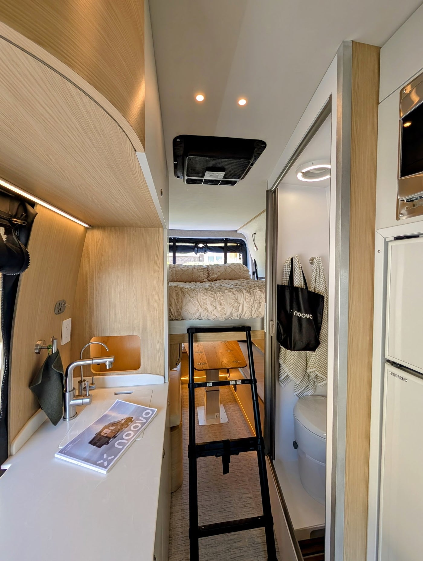 Inside a modern rv rental: a compact camper van featuring a kitchenette, elevated bed accessed by a ladder, and a small bathroom. — photo 10
