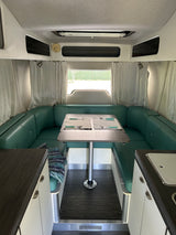 RV rental interior featuring a U-shaped dinette with teal leather seating and a wooden table, set for two.