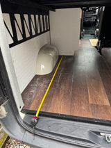 Measuring the spacious interior of an RV rental, showing wood-look flooring and white paneled walls with a tape measure.