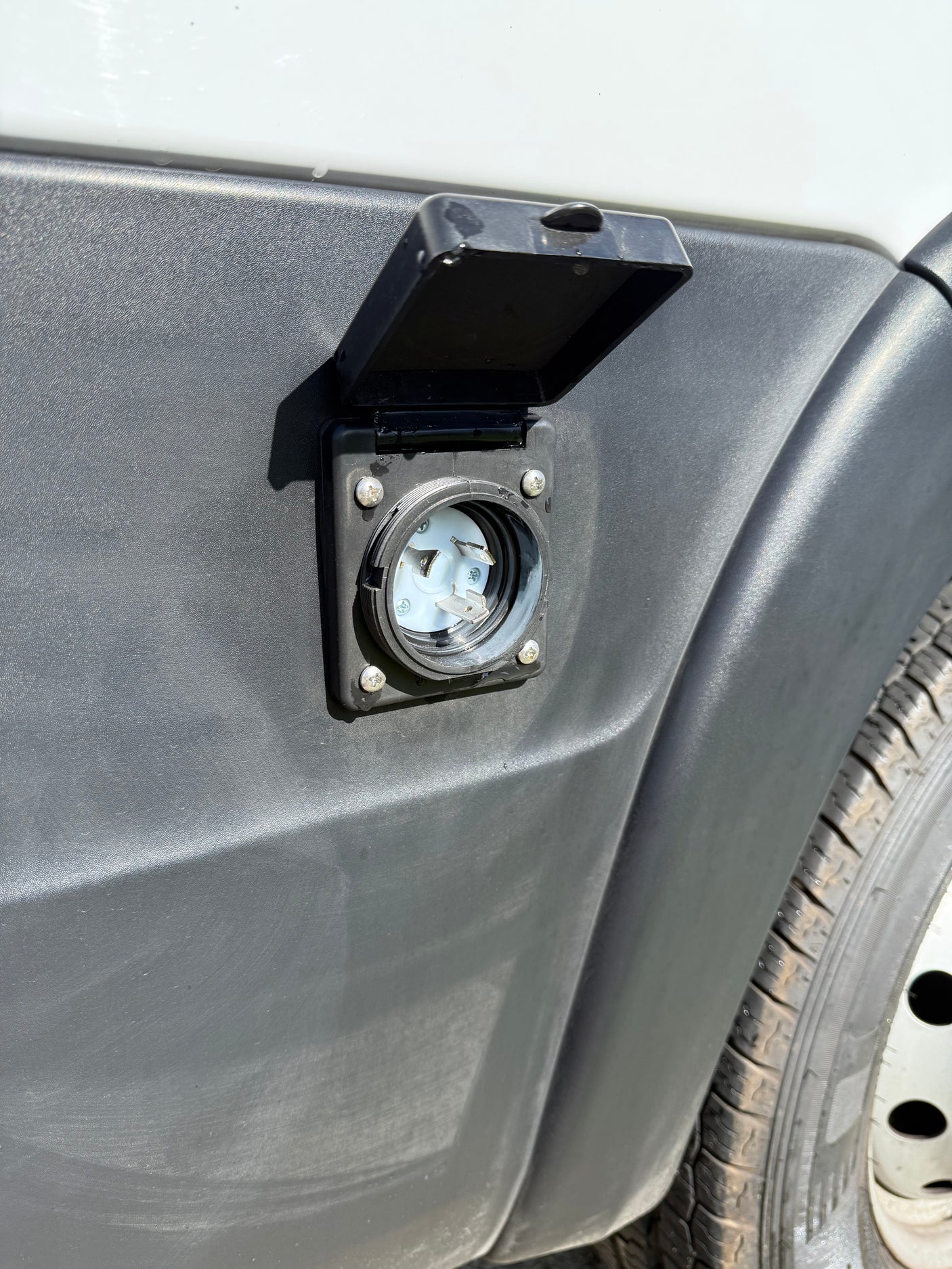 RV rental camper van's shore power inlet. Open, showing the electrical connection for external power hookup.