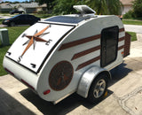 Unique white teardrop RV rental with solar panels and compass rose design, ideal for off-grid adventures.