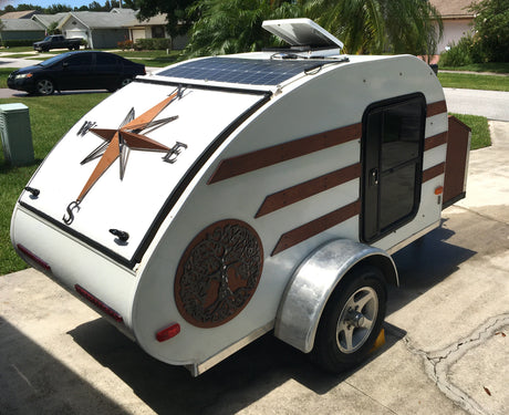 Unique white teardrop RV rental with solar panels and compass rose design, ideal for off-grid adventures.