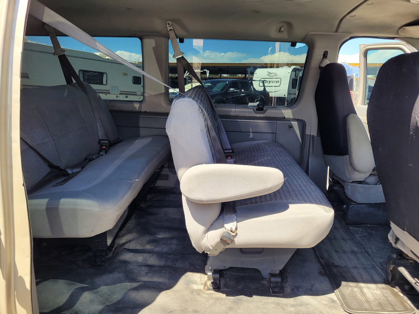 Interior of an RV rental van, showing spacious grey passenger seats. Through windows, RVs are parked under a blue sky. — photo 6