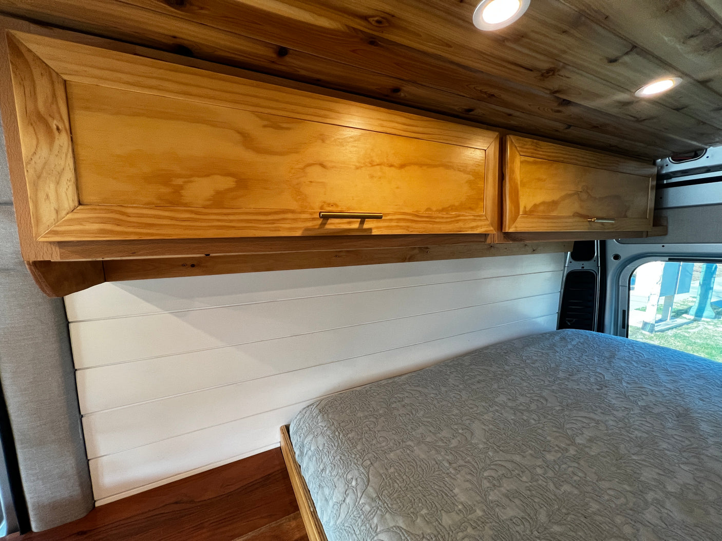 RV rental van interior: custom wood overhead cabinets, wood ceiling, white shiplap walls, and a comfy bed.