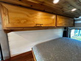 RV rental van interior: custom wood overhead cabinets, wood ceiling, white shiplap walls, and a comfy bed.