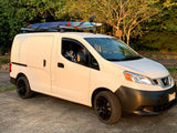 White Nissan cargo van with surfboard & foil on roof racks, black wheels. Ideal rv rental for adventure.
