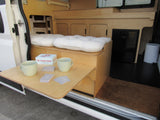 Cozy camper van interior of an RV rental, featuring a pull-out table with games, a comfortable bed, and a built-in fridge.