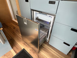 Inside an RV rental: modern kitchen with an open Isotherm fridge, light blue cabinets, wood floor, and fire extinguisher.