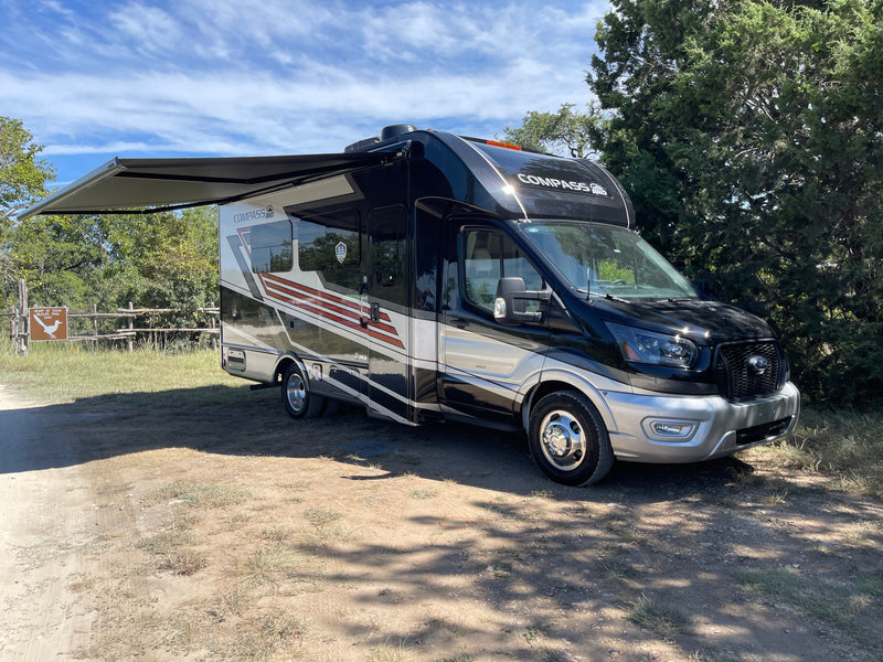 Explore nature with this Compass AWD RV rental. This black and silver motorhome is parked with its awning out near a wildlife trail. — photo 8