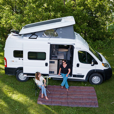 Enjoying an RV rental adventure! Two women relax by their white pop-top camper van in a grassy outdoor setting.