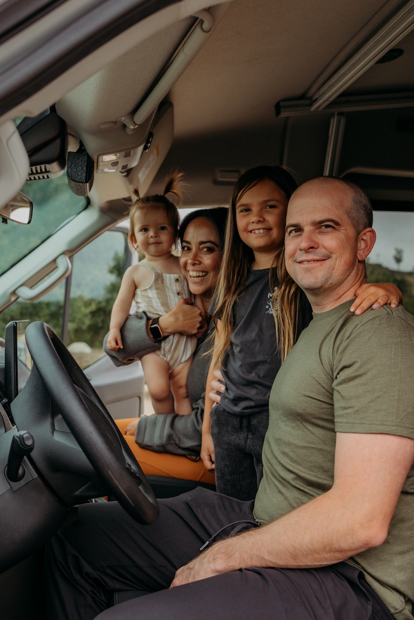 Smiling family of four (man, woman, two girls) inside their RV rental camper van, ready for travel adventures. — photo 6