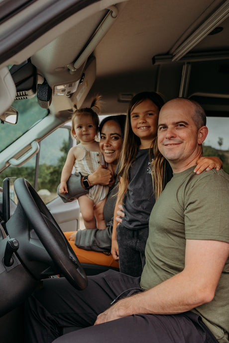 Smiling family of four (man, woman, two girls) inside their RV rental camper van, ready for travel adventures.