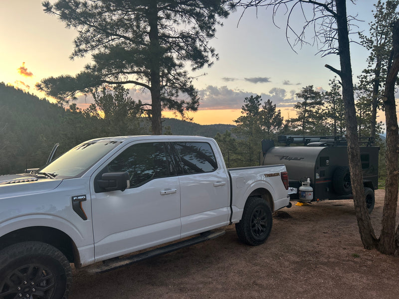 RV rental adventure: A white F-150 truck and off-road Flyer camper parked at sunset in the mountains among pine trees. — photo 2