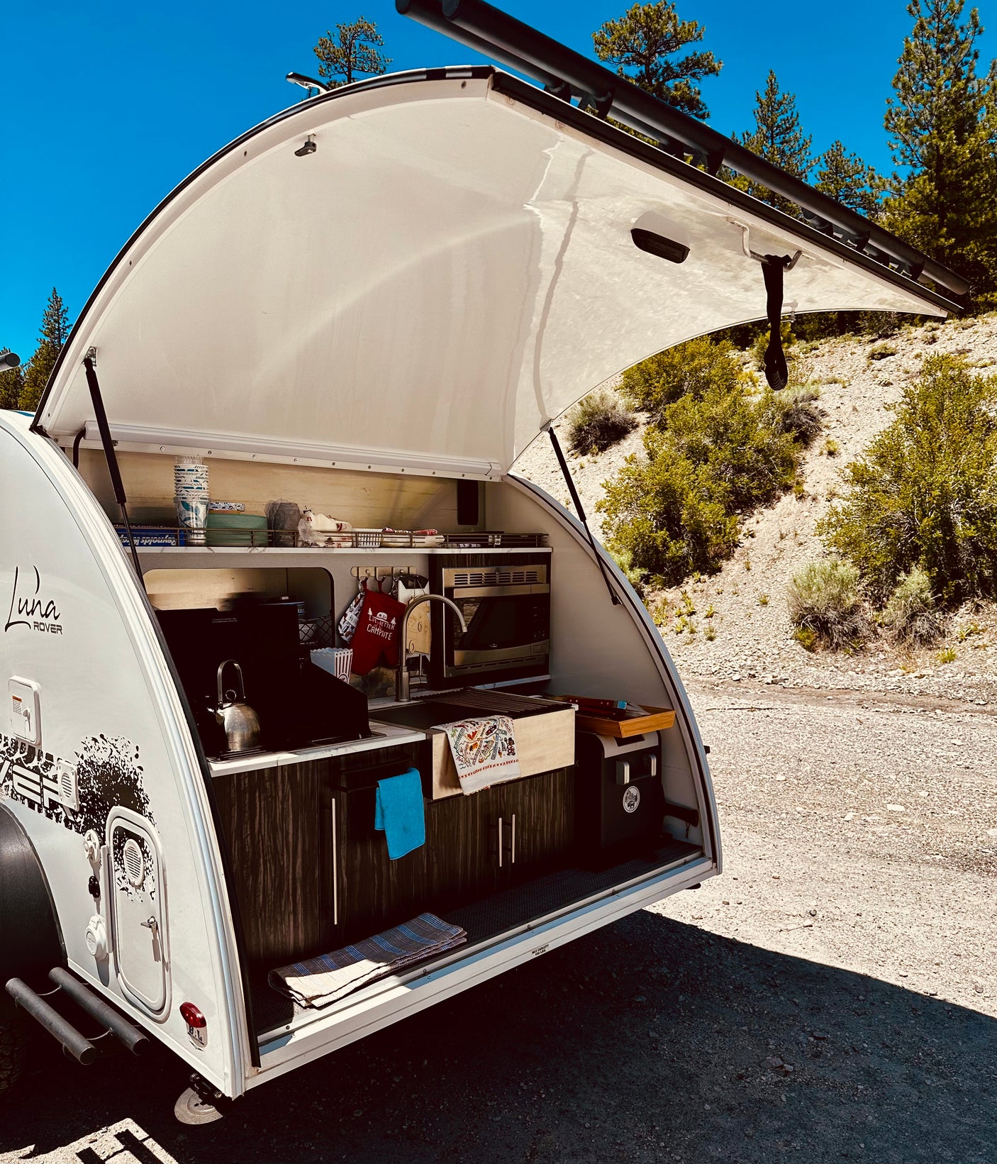 Explore nature with this Luna Rover teardrop RV rental. Its open rear hatch reveals a complete outdoor kitchen for scenic camping!