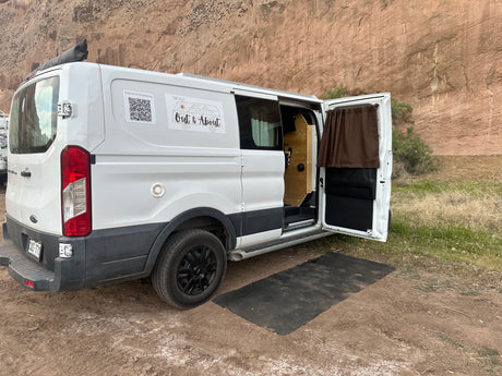 White custom RV rental camper van parked in nature with its side door open, inviting outdoor adventure.