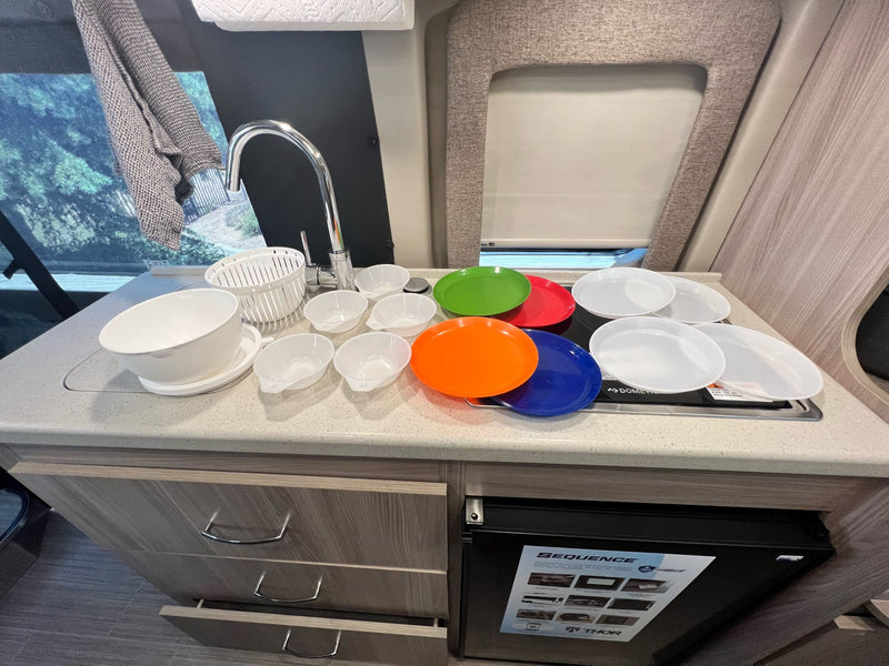 Explore an RV rental kitchen: counter, sink, cooktop, plates, bowls, and a compact fridge. Fully equipped for adventures! — photo 20