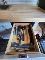 RV rental kitchen's open drawer with neatly stored utensils (forks, spoons, spatulas, knives) and cooking tools.