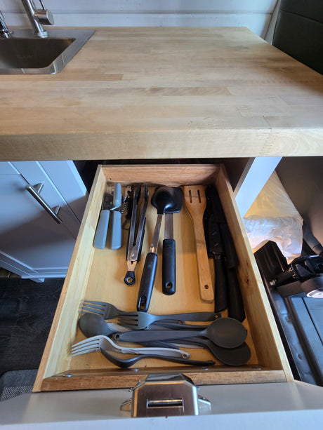 RV rental kitchen's open drawer with neatly stored utensils (forks, spoons, spatulas, knives) and cooking tools.