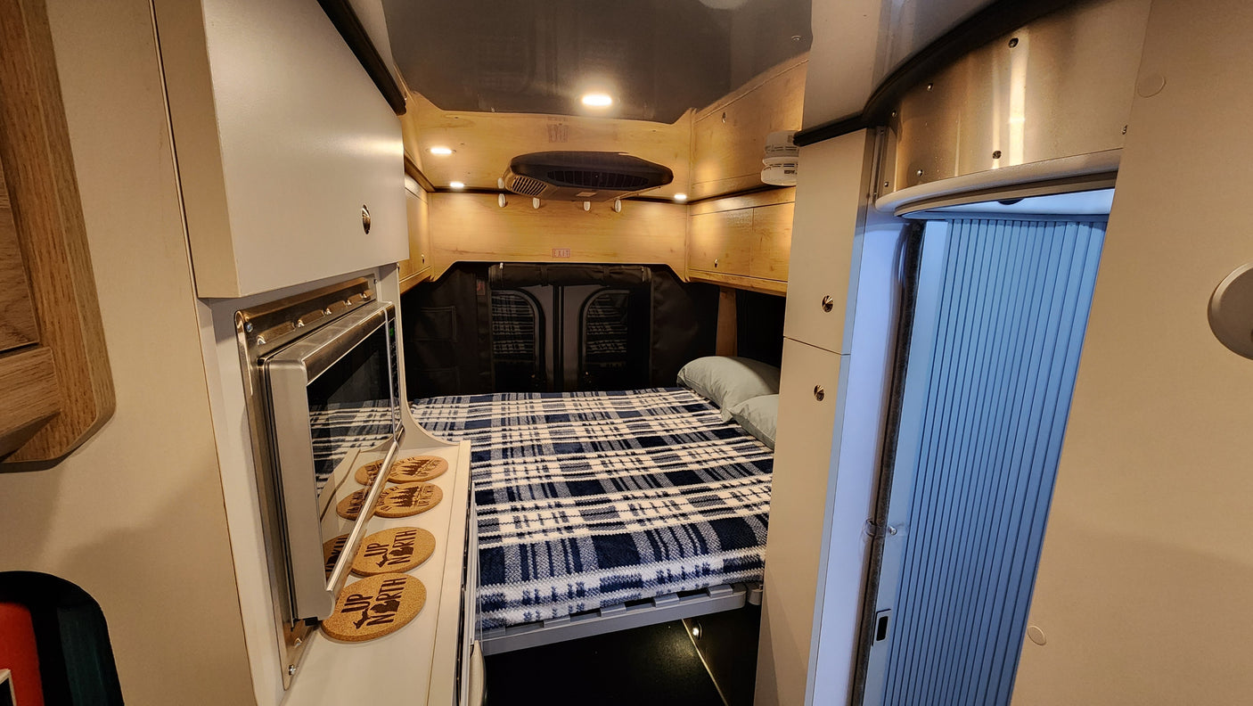 RV rental interior: cozy bed, compact kitchen with microwave, and smart storage for travel comfort.
