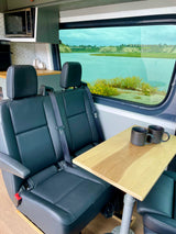 This cozy rv rental features two comfortable seats, a table with mugs, a kitchenette, and a scenic window view of a lake.