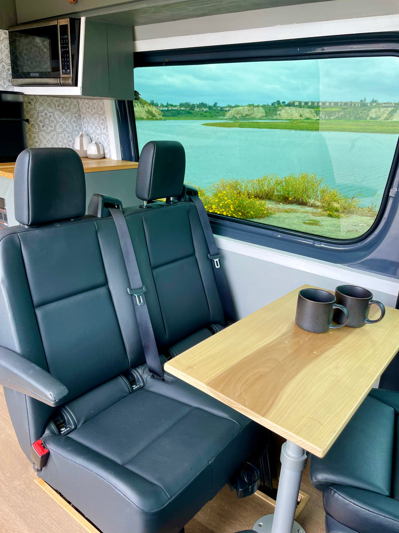 This cozy rv rental features two comfortable seats, a table with mugs, a kitchenette, and a scenic window view of a lake. — photo 15