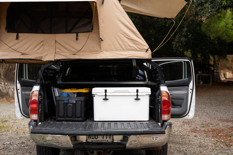 This pickup truck, perfect for an RV rental adventure, sports a tan rooftop tent, a cooler, and storage in its open bed.