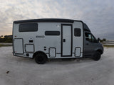 Modern Winnebago EKKO RV rental parked on sandy ground by water under a cloudy sky, ideal for outdoor adventures.