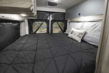 This RV rental's comfy bedroom features a large bed, overhead storage, and rear windows with a nature view.