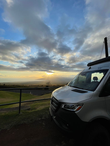 White RV rental van parked at a scenic overlook, capturing a beautiful sunset over the ocean. Ideal for van life adventures.