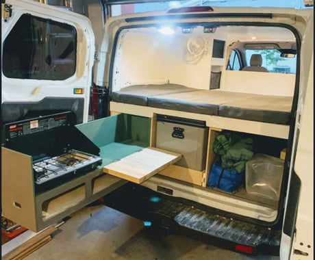 This RV rental features a compact camper van conversion with a bed, pull-out stove, fridge, and storage for mobile living.