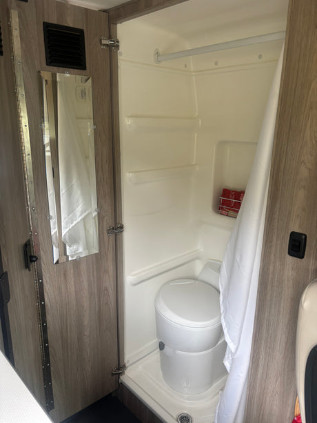 Inside an rv rental, a compact bathroom features a shower stall with a toilet, a shower curtain, and a mirror on the door.