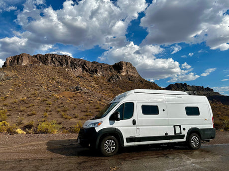  ready for your next rv rental adventure.|White Winnebago Solis rv rental parked on a desert road. Rocky mountains and a cloudy blue sky complete this scenic road trip.|Cozy RV rental camper van bedroom. Breakfast in bed with juice and berries. Pillows and storage complete the cozy camping setup.|Well-equipped rv rental interior: modern camper van kitchen with stove