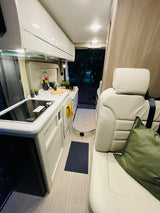 Step inside this inviting RV rental. Features a sleek kitchenette with cooktop and sink, comfortable seating, and cozy lighting.