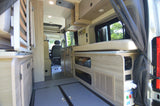 Interior of an RV rental, showing a functional layout with wood cabinetry, cushioned seating, and ample storage.