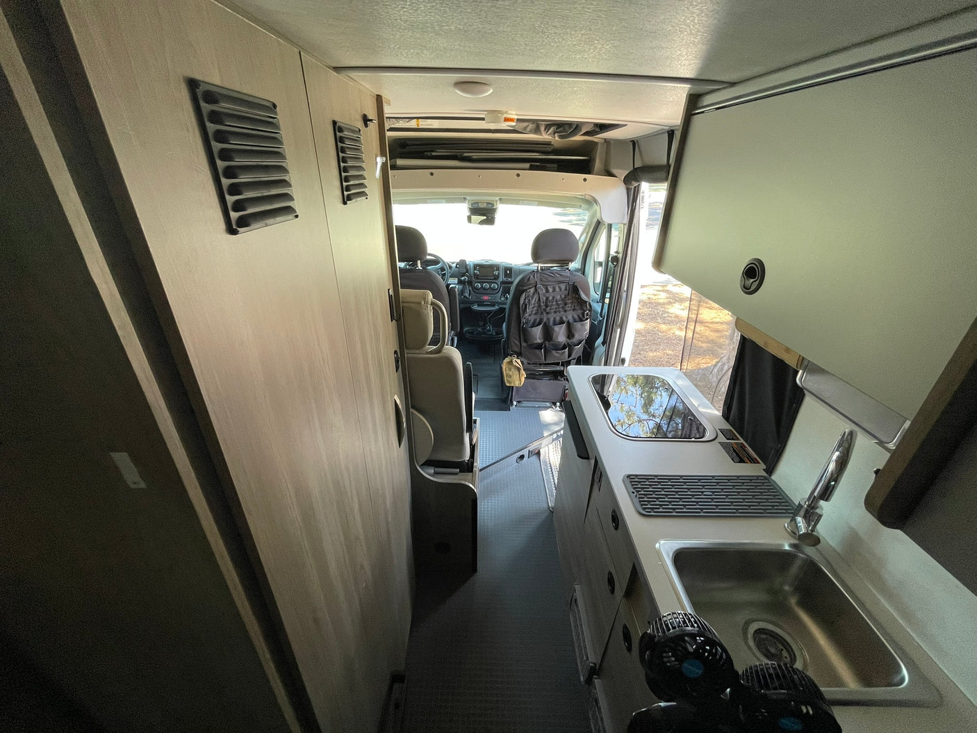 RV rental interior: View from the rear, showing a compact kitchen with sink and stovetop, leading to the driver's cabin.