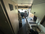 RV rental interior: View from the rear, showing a compact kitchen with sink and stovetop, leading to the driver's cabin.