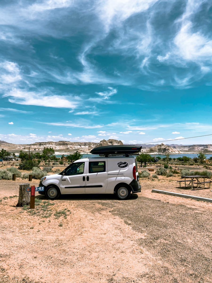 White RV rental camper van at lakeside campsite 3-63, surrounded by arid landscapes under a blue sky.