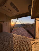 Inside an rv rental: a cozy bed overlooking a breathtaking desert sunset and mountain range. Ideal for off-grid camping.