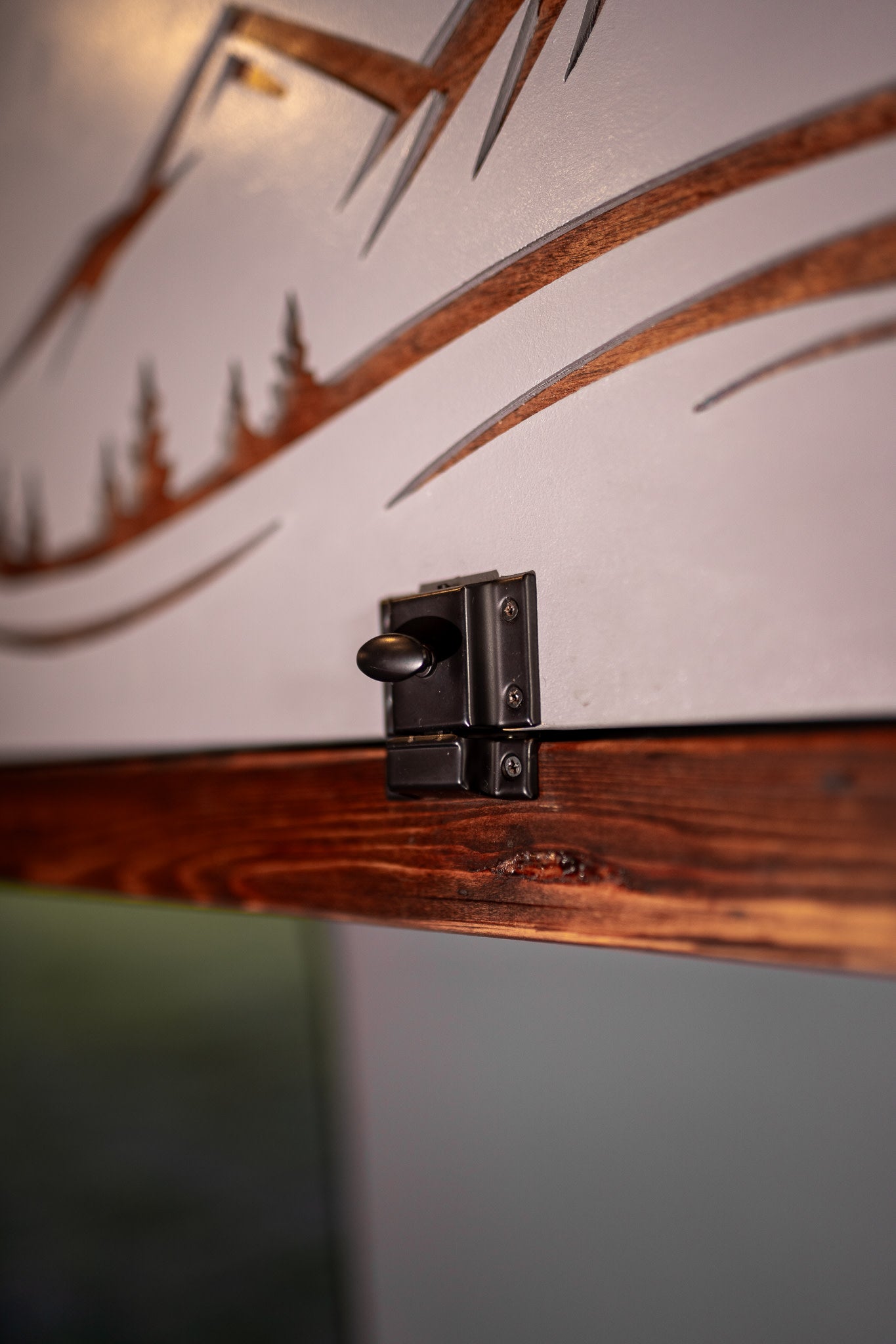 Close-up of an RV rental cabinet latch, securing a gray panel with mountain cut-outs to dark wood. Perfect for adventure storage.