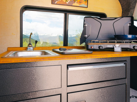 RV rental kitchen: cozy interior with sink, Coleman stove, and stunning mountain views.