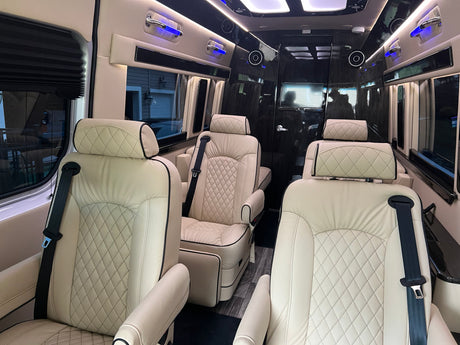 Inside a luxury rv rental: plush cream quilted seats with black trim, blue accent lights, and sleek dark paneling create a lavish cabin.