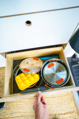 RV rental compact kitchen storage: Hand opens drawer revealing organized nesting pots, pans & ice mold.