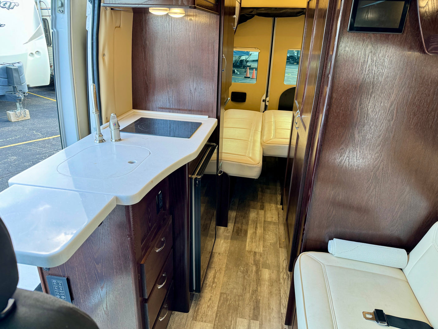 View inside an rv rental, showcasing a kitchen with sink & cooktop, dark wood cabinetry, and light seating.