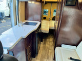 View inside an rv rental, showcasing a kitchen with sink & cooktop, dark wood cabinetry, and light seating.