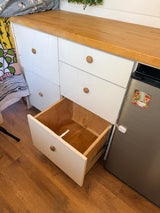 RV rental kitchenette: A wooden countertop, white drawers (one open), and a mini-fridge, all on a wood floor.