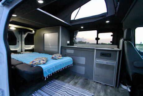 Spacious camper van interior for rv rental, showing a comfy bed, compact kitchen, and pop-top for bright adventures.