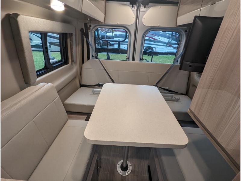 An RV rental interior reveals a modern dining area with bench seating, a table, mounted TV, and large windows.