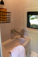 Compact sink area in an rv rental, featuring a modern pull-out faucet, white basin, and a window. Convenient for travel.