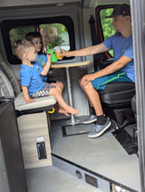 Inside a spacious rv rental, a dad gives drinks to two happy boys seated at a table.