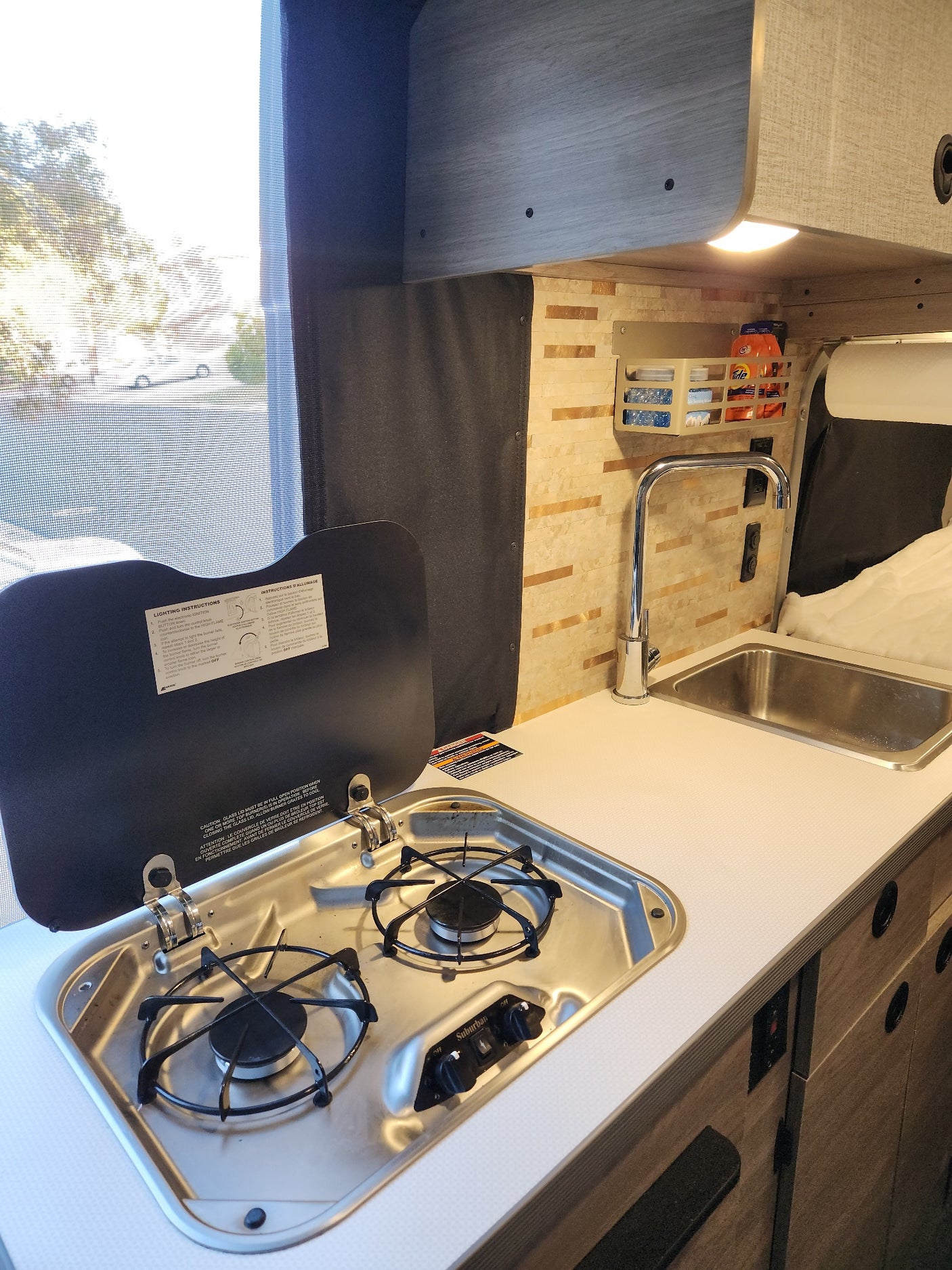 RV rental: Bright kitchen area with a two-burner stovetop, sink, counter space, and window view for your travels.